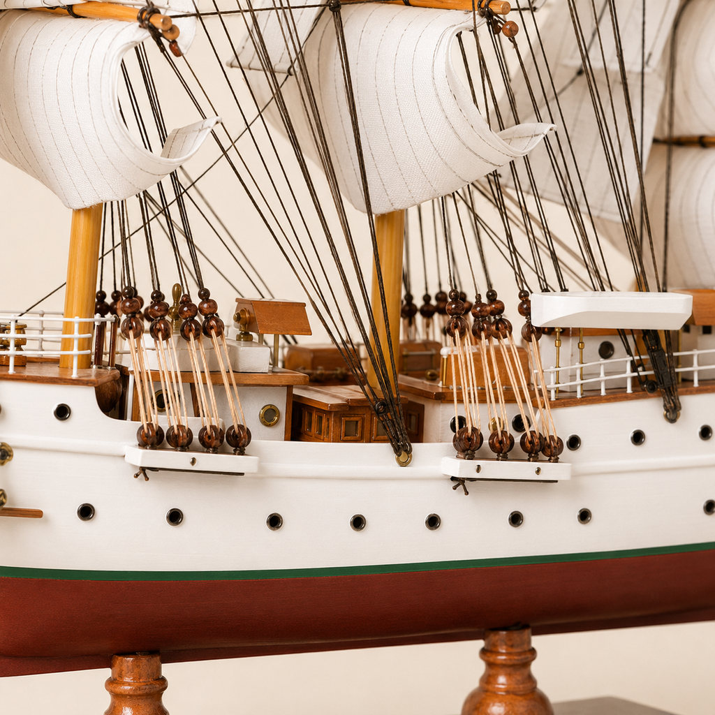 Close-up of the Sørlandet model ship showing textured white sails, black rigging lines, wooden pulleys, deck cabins, railings, portholes and handcrafted nautical details.