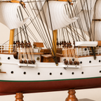 Close-up of the Sørlandet model ship showing textured white sails, black rigging lines, wooden pulleys, deck cabins, railings, portholes and handcrafted nautical details.