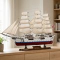 Large handcrafted Norwegian tall ship model displayed on a wooden cabinet in a modern interior, featuring cream fabric sails, detailed rigging, white hull, red lower hull and Norwegian flag.
