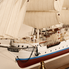 Close-up of the handcrafted tall ship model showing textured fabric sails, rope rigging, wooden pulleys, deck railings, anchor chains, portholes and detailed deck fittings.