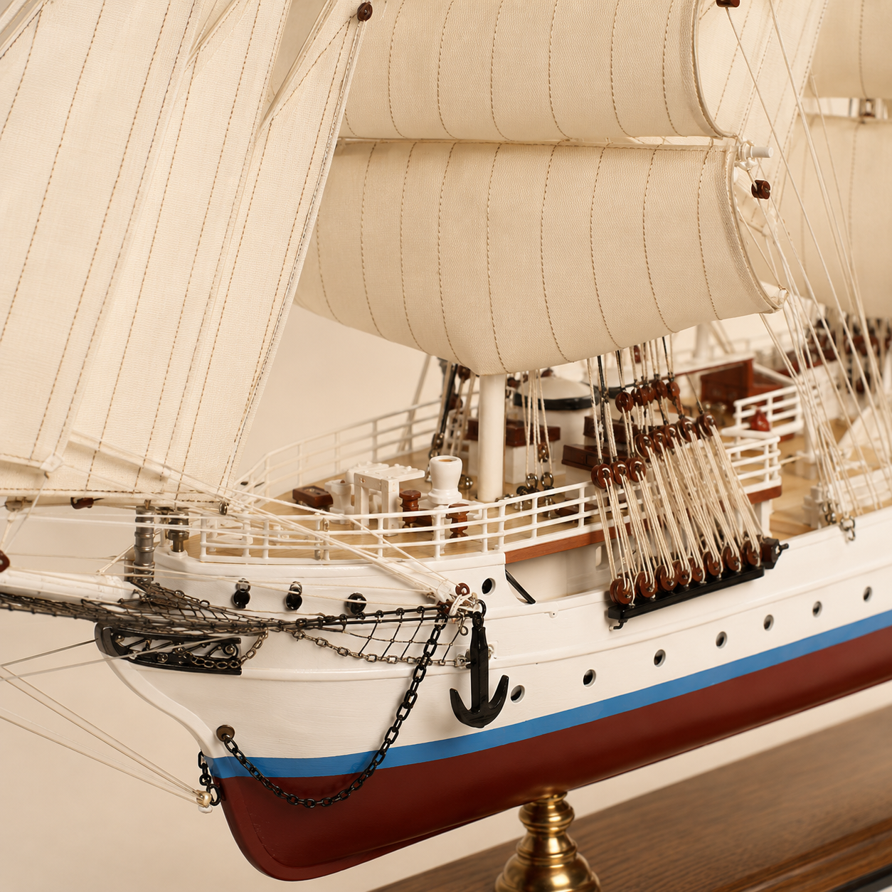 Close-up of the handcrafted tall ship model showing textured fabric sails, rope rigging, wooden pulleys, deck railings, anchor chains, portholes and detailed deck fittings.