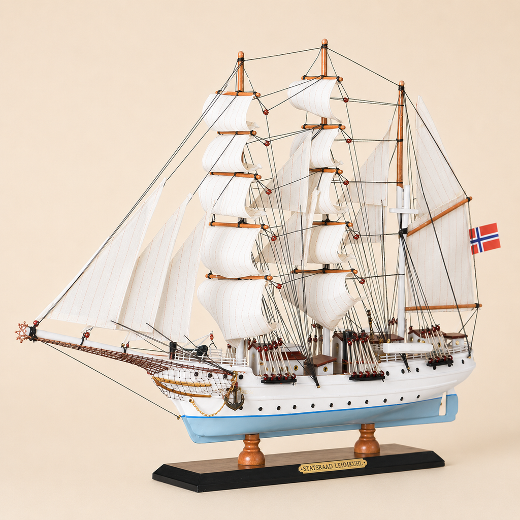 Front 45-degree view of the Statsraad Lehmkuhl ship model on a cream background, showing the bow, layered white fabric sails, detailed rigging, light blue hull and Norwegian flag.