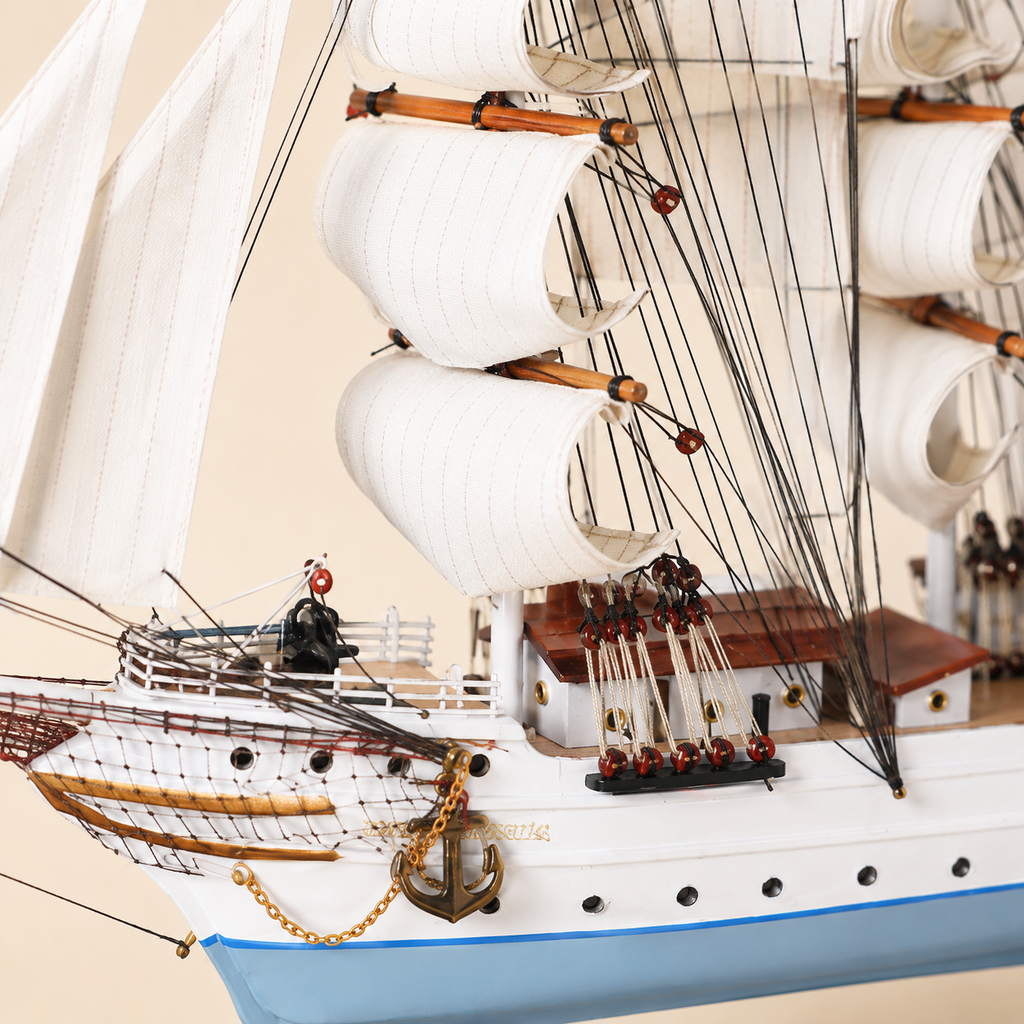 Close-up of the Statsraad Lehmkuhl model ship showing textured white sails, wooden masts, black rigging, pulleys, deck cabins, railings, anchor chain and handcrafted hull details.