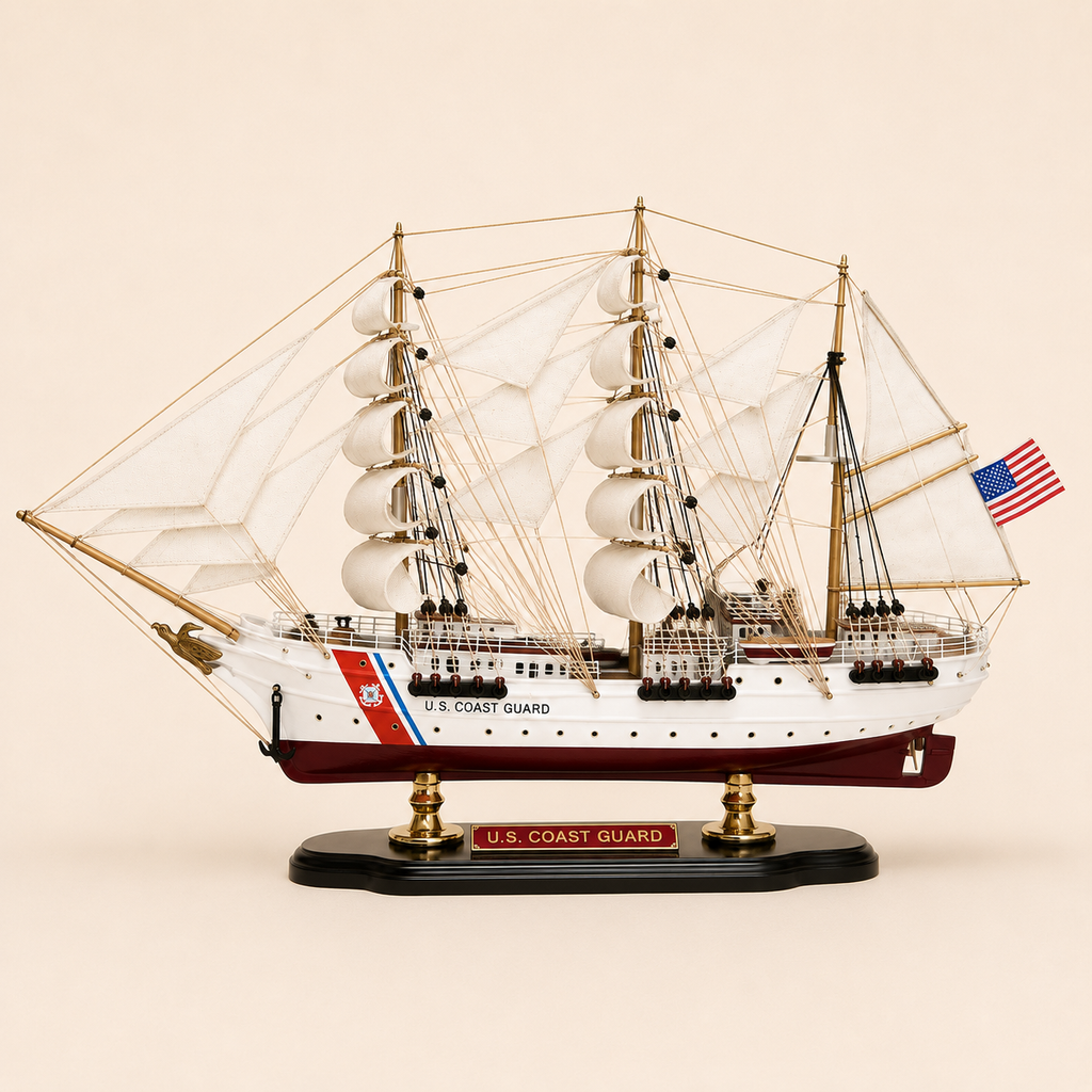 Side view of the U.S. Coast Guard three-masted ship model featuring white fabric sails, detailed rope rigging, white hull, burgundy lower hull, Coast Guard markings and black presentation base.