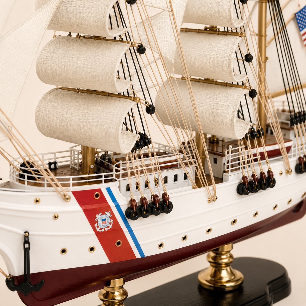 Close-up of the U.S. Coast Guard model ship showing textured white sails, black and tan rigging, wooden pulleys, deck railings, cabins, portholes, Coast Guard emblem and handcrafted hull details.