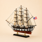 Rear 45-degree view of an American wooden sailing ship model showing the stern, rear deck, U.S. flag, cream sails, detailed rigging, decorative stern windows and black display stand.