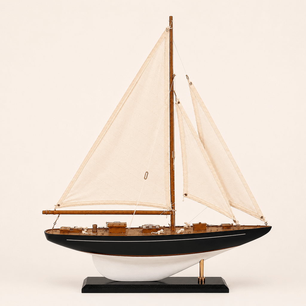 Modello di barca a vela americana a un albero, vista laterale, con vele bianche, scafo blu navy, ponte in teak e finiture in ottone