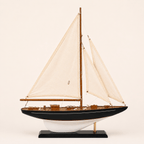 Modello di barca a vela americana a un albero, vista laterale, con vele bianche, scafo blu navy, ponte in teak e finiture in ottone