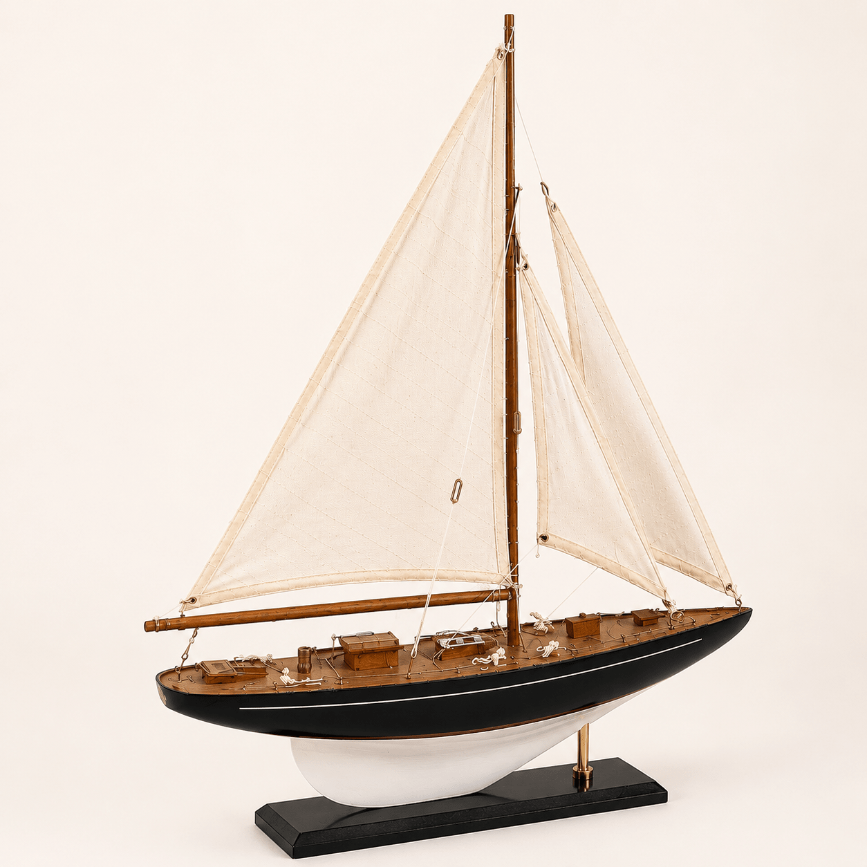 Modello di barca a vela americana a un albero, vista frontale a 3/4, con vele bianche, scafo blu navy, ponte in teak e finiture in ottone