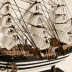 Primer plano del modelo de gran velero Amerigo Vespucci de la Marina italiana, mostrando nudos de densa jarcia negra, textura de velas blancas de aparejo cuadrado, vergas de madera, casco negro y blanco a rayas con puntos blancos y placa dorada AMERIGO VESPUCCI sobre base negra