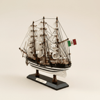 Vista posterior de tres cuartos del modelo de gran velero Amerigo Vespucci de la Marina italiana sobre fondo crema, mostrando estructura de jarcia de tres mástiles, velas blancas de aparejo cuadrado, bandera de la Marina italiana en popa, casco negro y blanco a rayas y base negra con placa dorada AMERIGO VESPUCCI