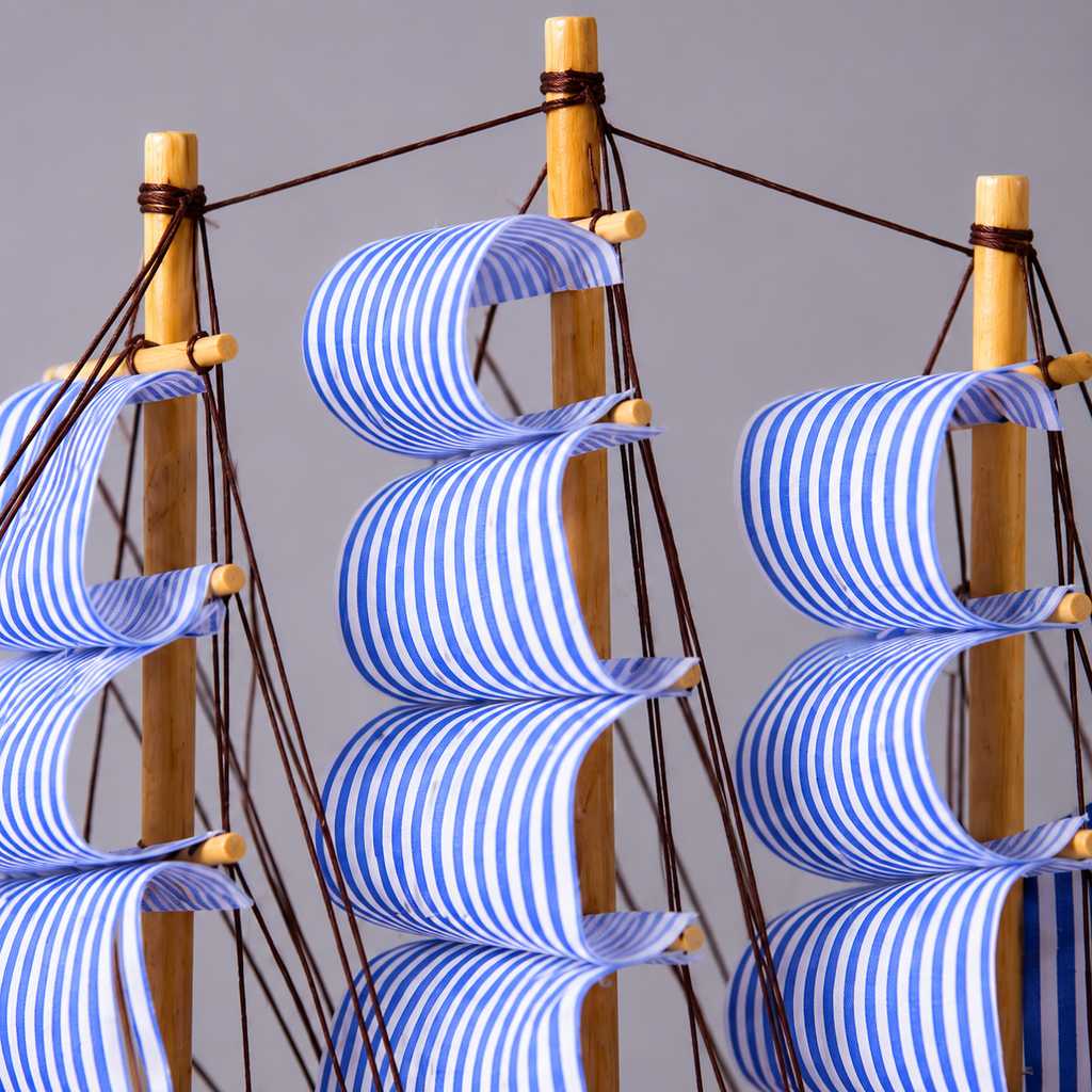Model ship with blue and white striped sails against a gray background