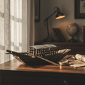 Chinese river junk model displayed on a wooden desk beside a brass compass and antique map, with natural window light and globe in background