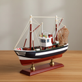 Handcrafted American shrimp boat wooden ship model on warm wooden desk – navy blue hull with white stripe, white wheelhouse, red outrigger booms, white rope rigging, metal fishing net, mahogany base with brass feet, coastal nautical home decor