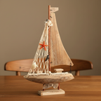 Handcrafted Mediterranean sailboat wooden ship model displayed on warm wooden desk – macramé rope net sail with orange starfish and seashell decorations, weathered driftwood hull, coastal nautical home decor